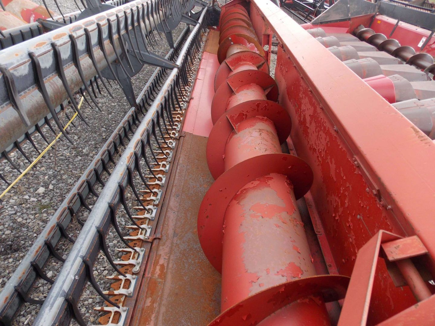 Close-up of red and gray agricultural machinery with rotating augers and conveyor chains
