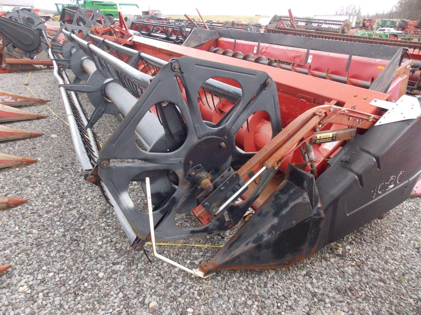 Damaged red and black combine harvester header лежing on gravel in an equipment yard