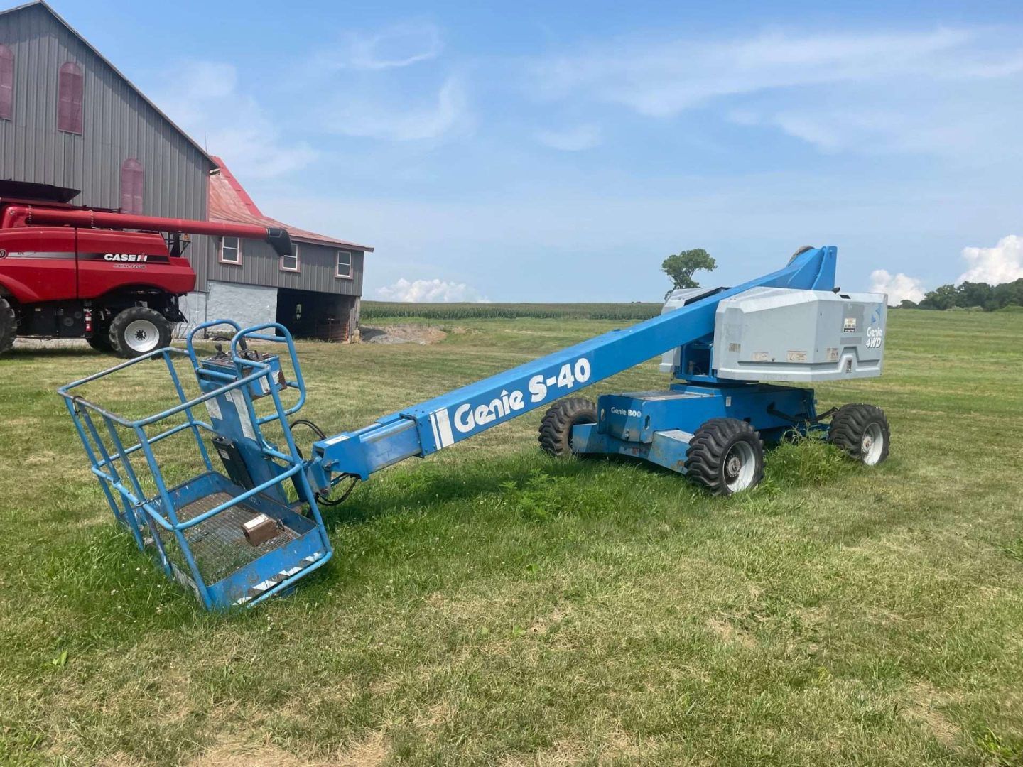 Blue Genie GS-80 boom lift parked on grass near a red barn under a clear sky
