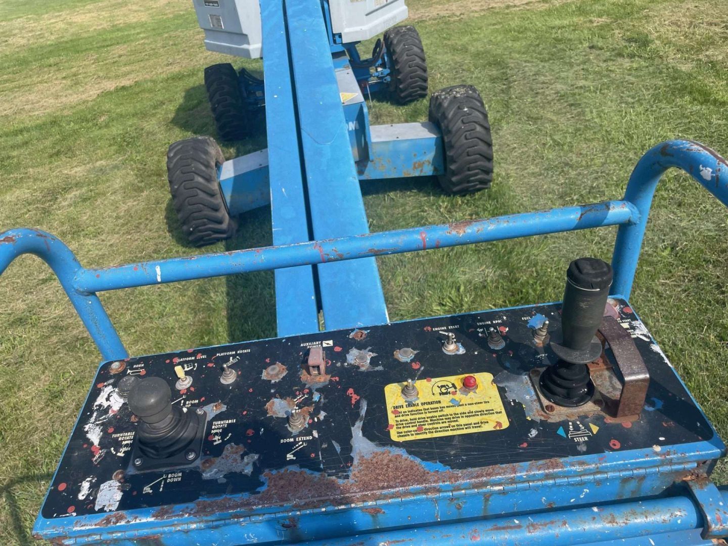 Blue farm machine hitch and control panel on grass, with worn black metal and large tires visible.