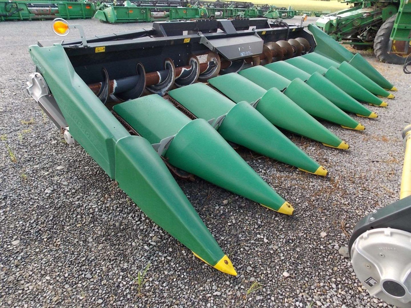 Green corn header with pointed snouts parked on gravel outdoors
