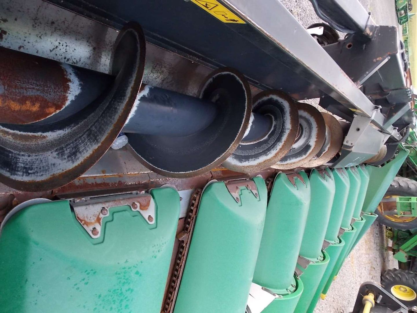 Row of green industrial buckets beneath a rusted metal machine, close-up view