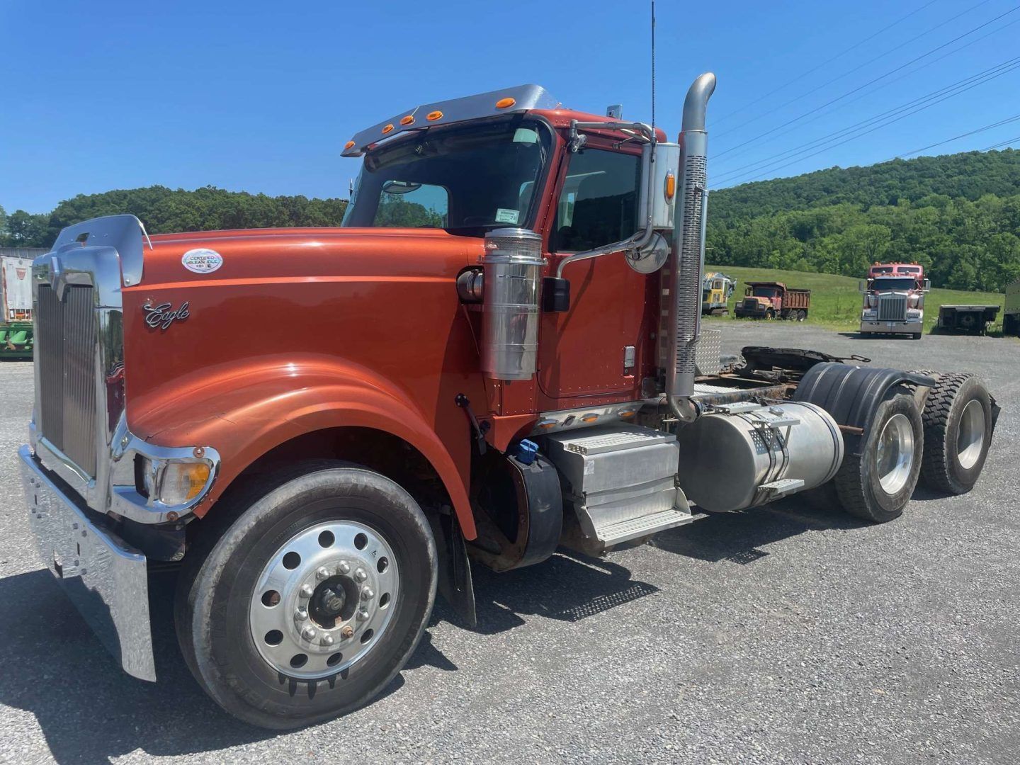 Red semi truck parked on a gravel lot with green hills in the background