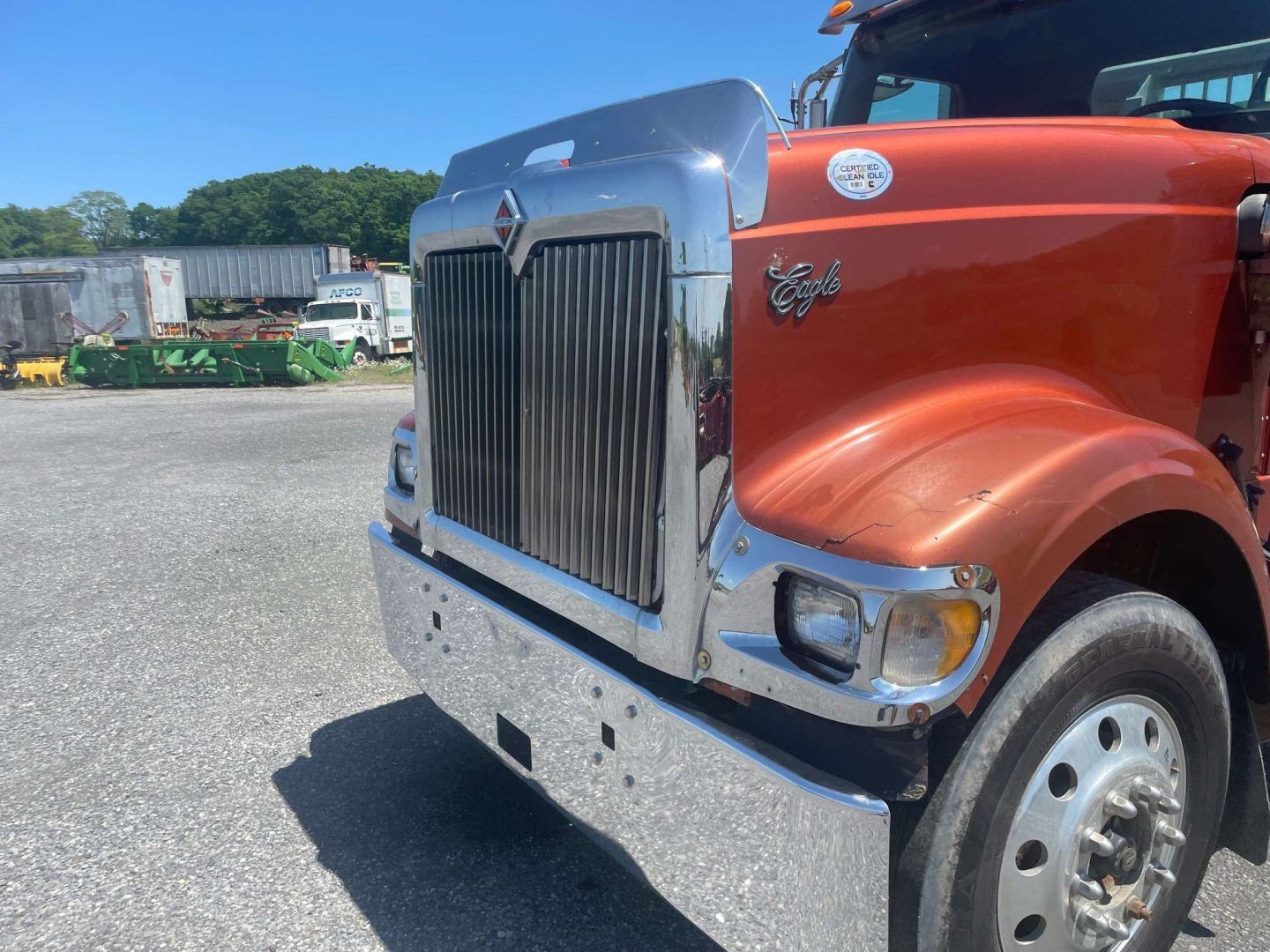 Red semi-truck with chrome grille parked on gravel lot under a blue sky