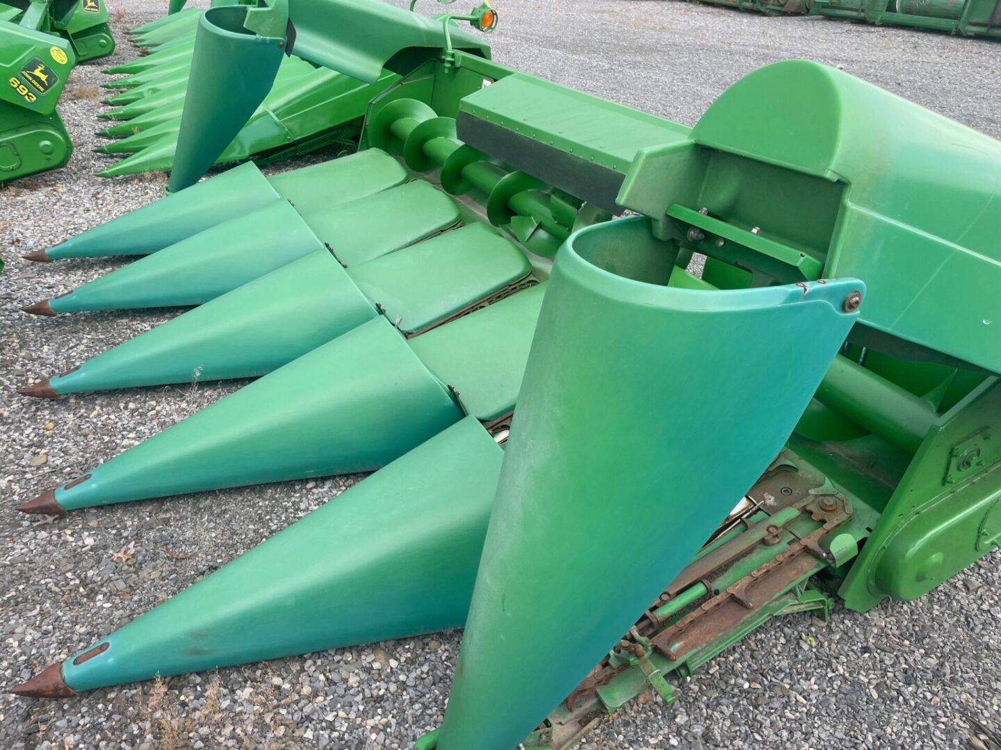 Green corn harvester header with pointed metal gathering cones and cutting bars displayed on gravel