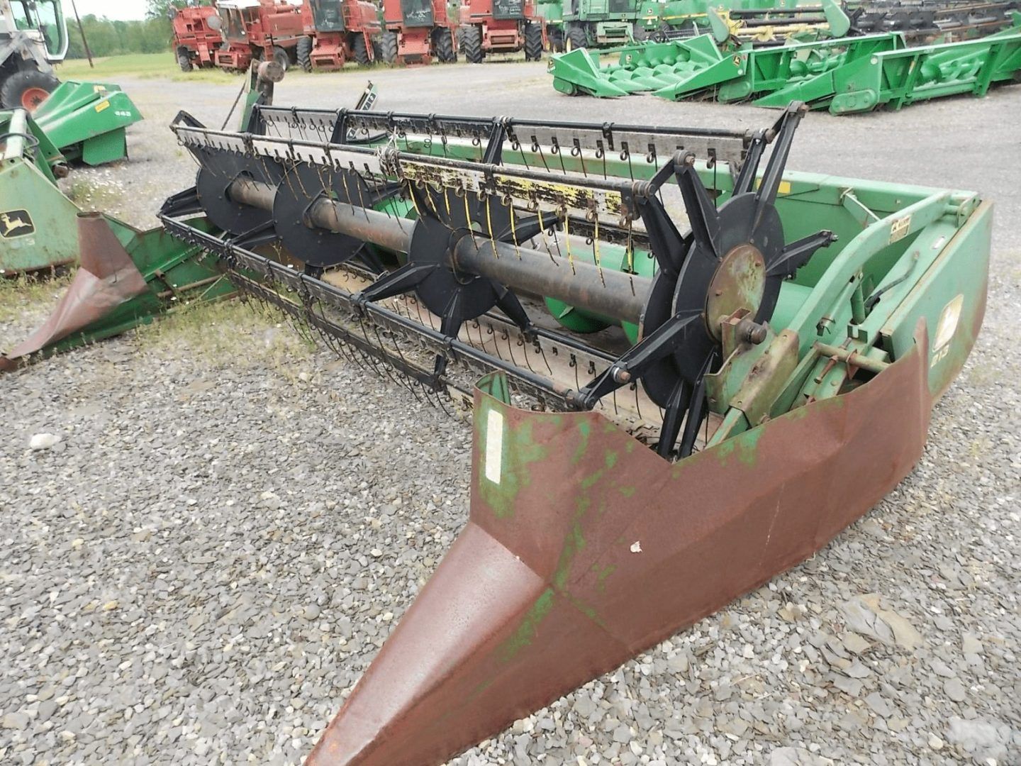Green and brown farm harvester header with black reel, parked on gravel lot