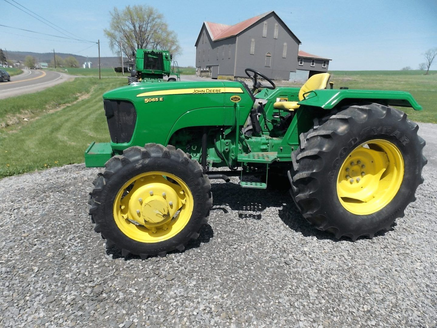 Green tractor with yellow wheels parked on gravel beside a rural house.