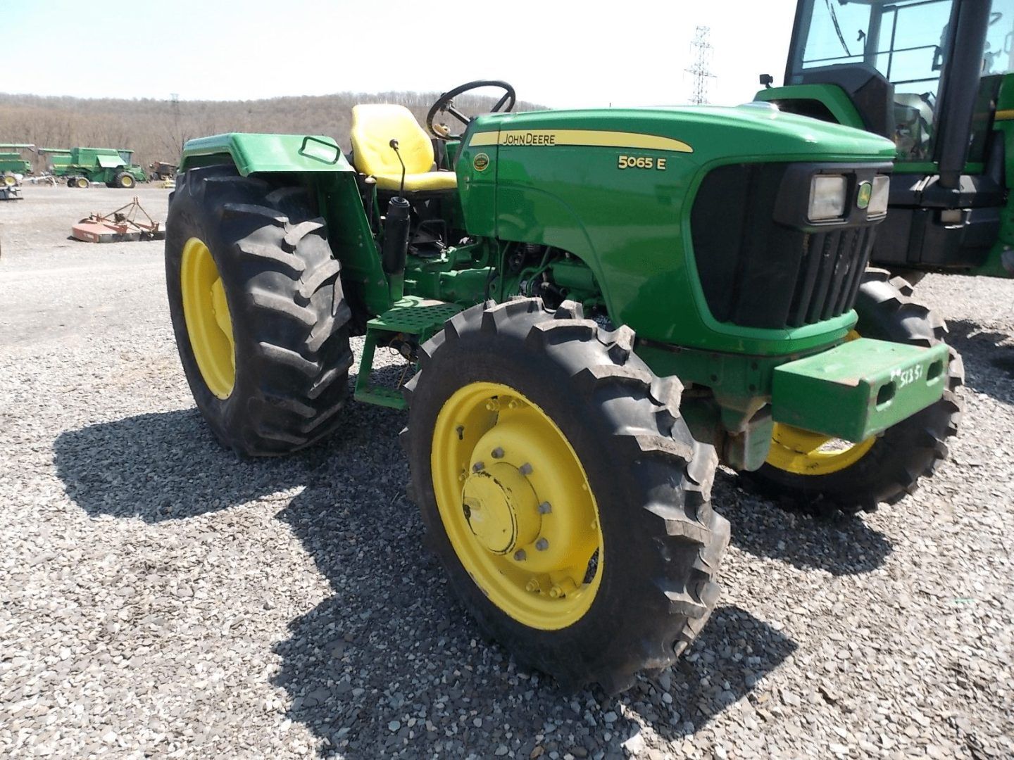Green John Deere tractor with yellow wheels parked on a gravel lot.