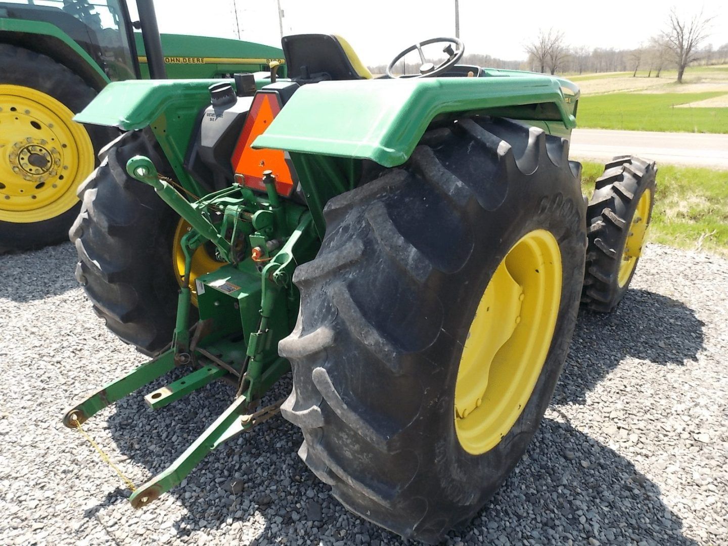 Rear view of a green tractor with large black tires and yellow rims on gravel.