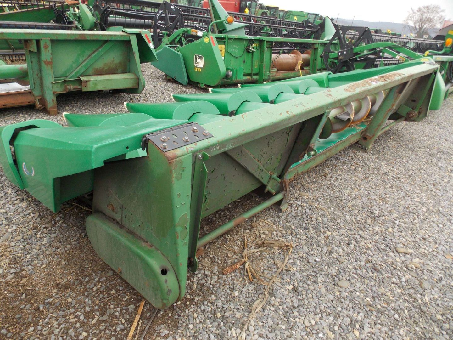 Green agricultural implement on gravel lot, with hydraulic arms and metal frame.