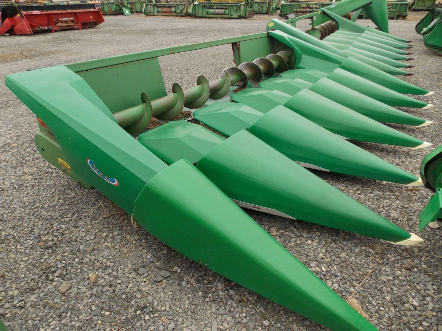Green corn header attachment with pointed rows of metal crop dividers on a gravel lot