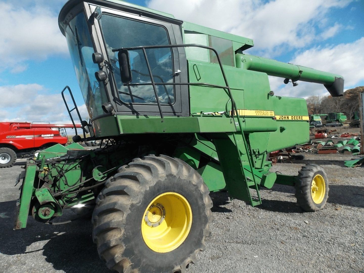 Green John Deere combine harvester on gravel lot under cloudy sky