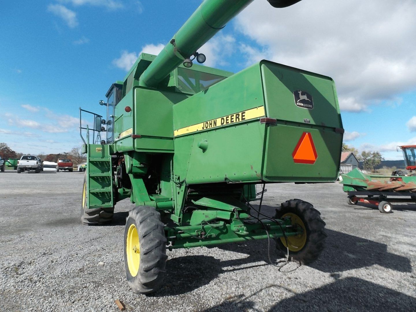 Green combine harvester with yellow wheels in a gravel lot, viewed from the rear side.