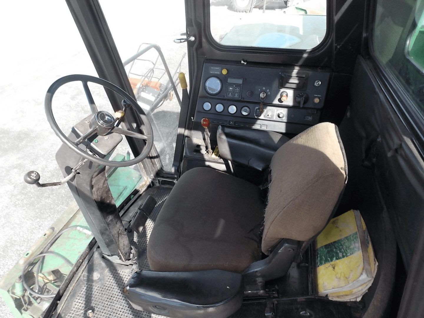 Inside a vehicle cab, a steering wheel, control panel, and two seats are visible.