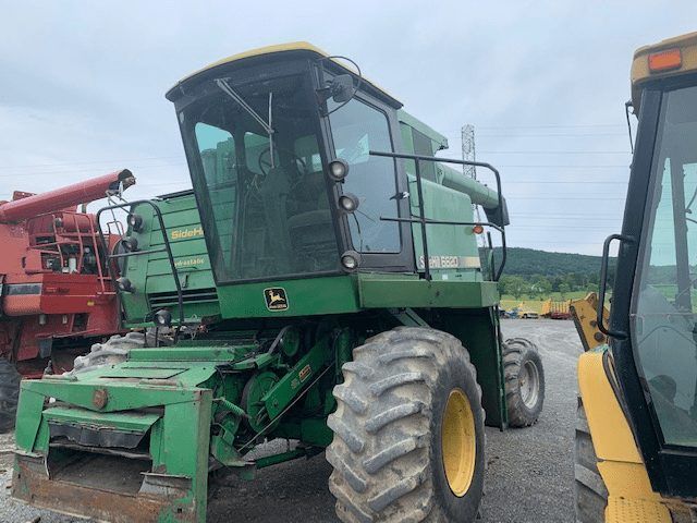 Green agricultural combine harvester parked outdoors beside another machine.