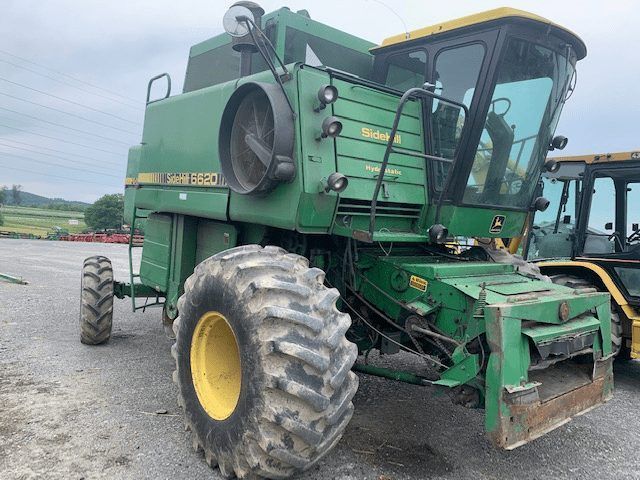 Green agricultural machine with large tires parked on a paved lot, side view