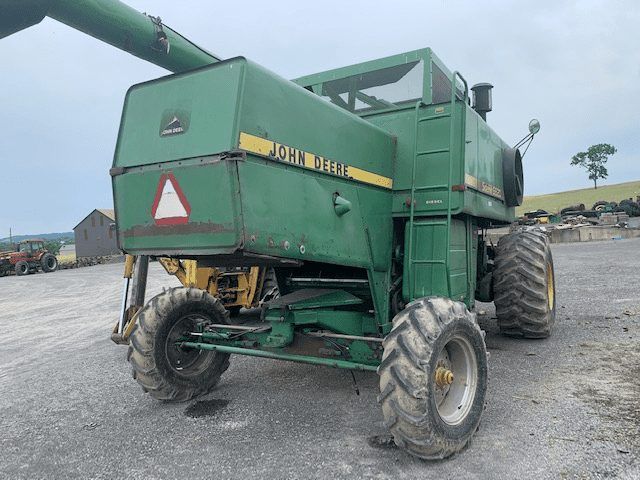 Green combine harvester with large tires parked on a gravel lot.