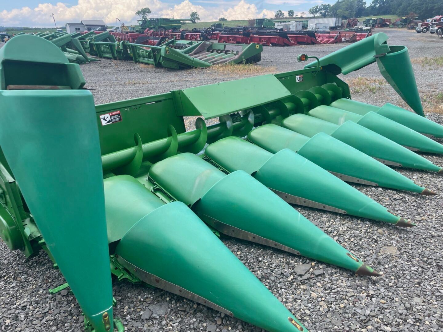 Green corn header with pointed rows of harvesting cones on a gravel lot