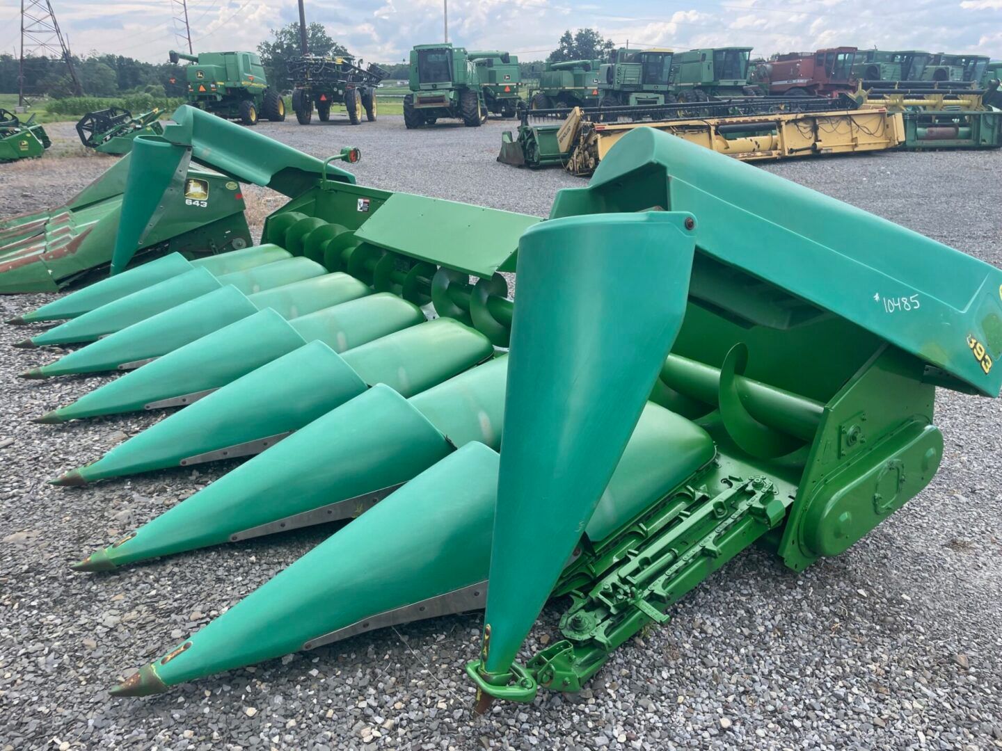 Green agricultural combine header with pointed crop pickup tines parked on a gravel lot