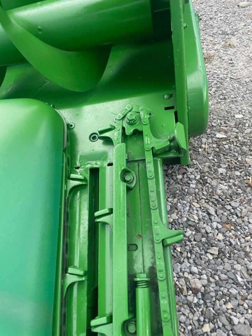 Close-up of a green metal machine part with gears and bolts on gravel.