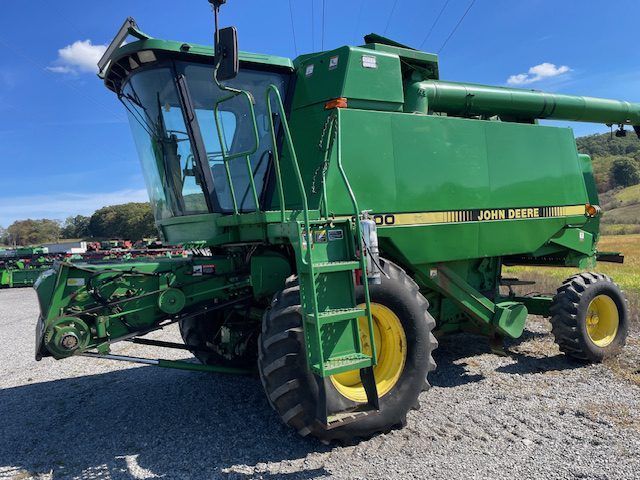 Green John Deere combine harvester parked on gravel lot under a clear blue sky