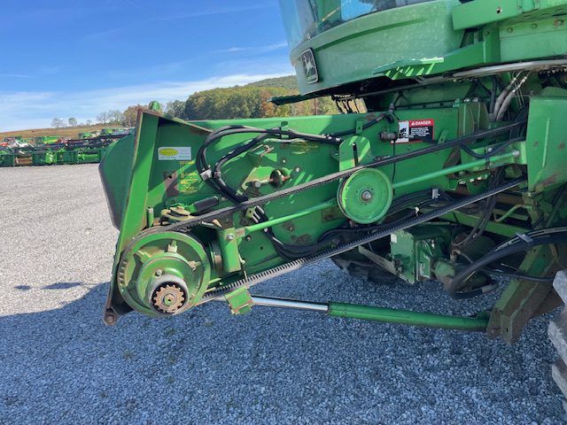 Close-up of green farm machinery with belts and gears parked on a gravel lot