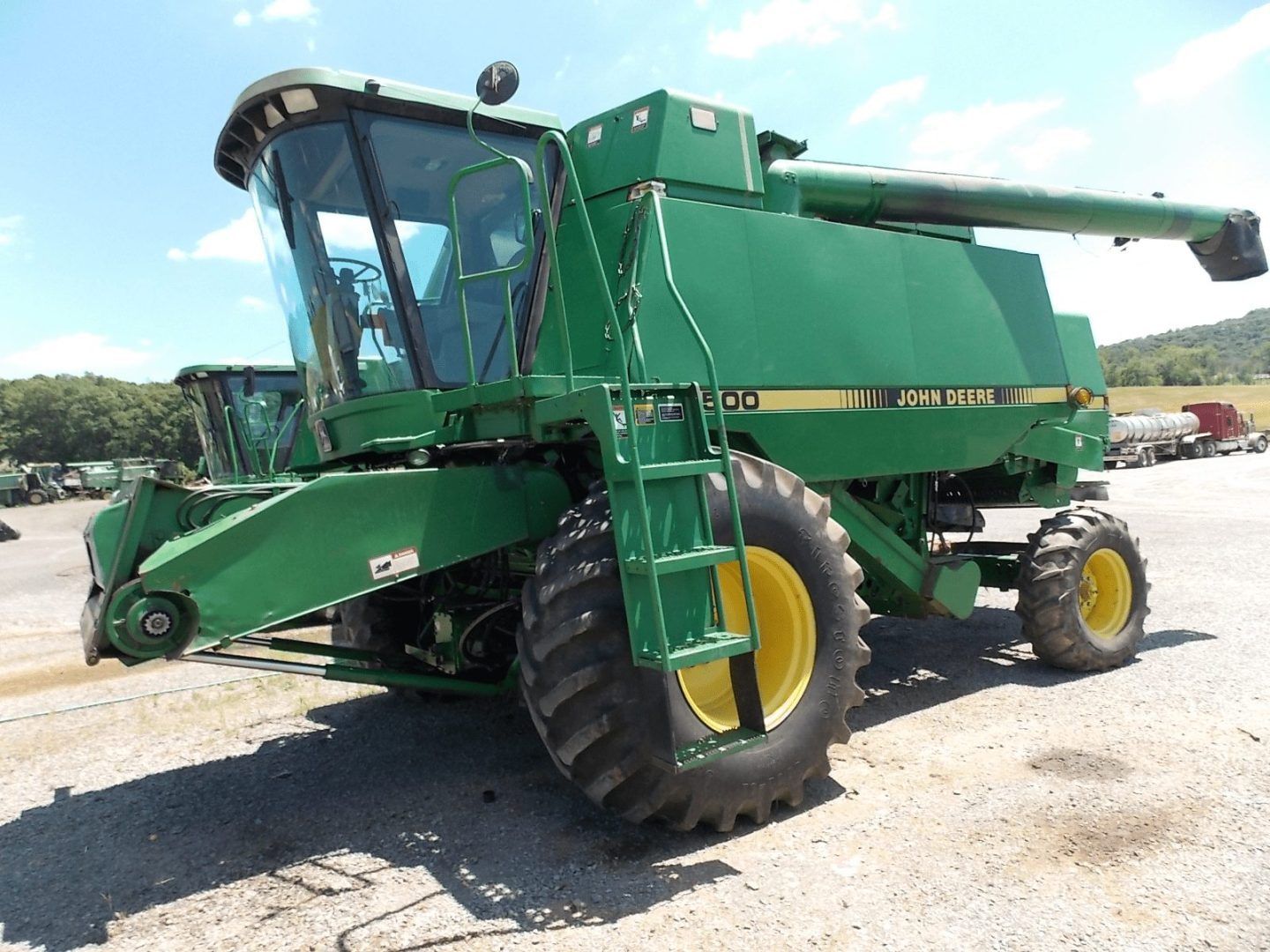 Green combine harvester on a gravel lot, shown from the front-left side.