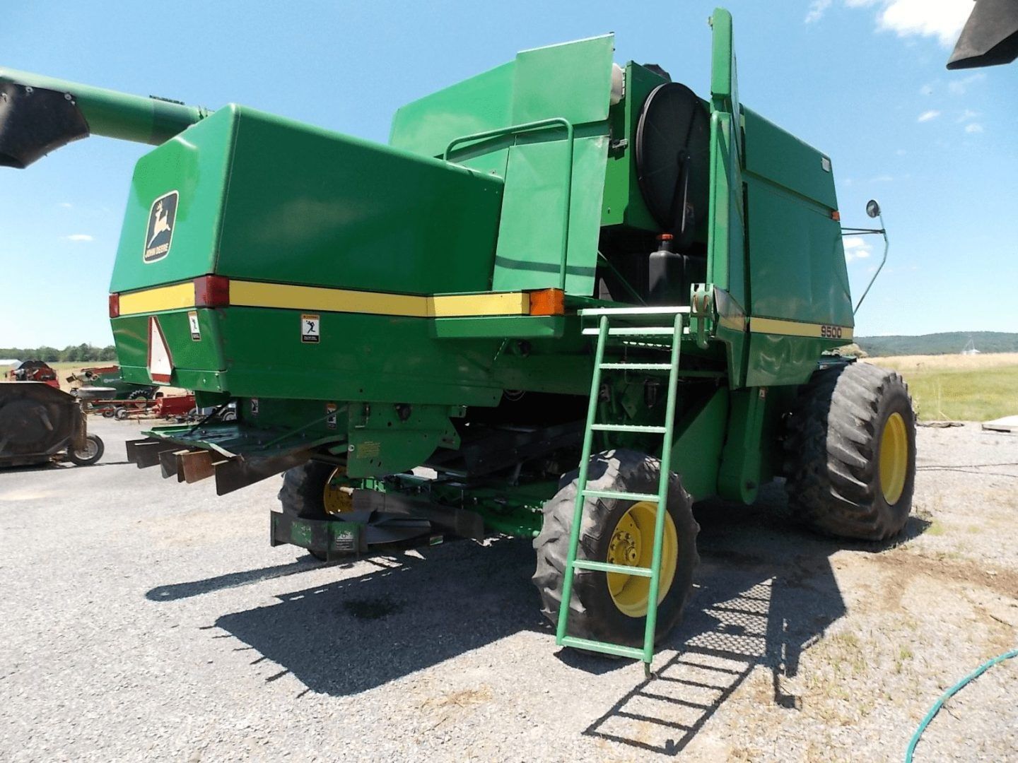 Green combine harvester with rear ladder parked on gravel under a blue sky.