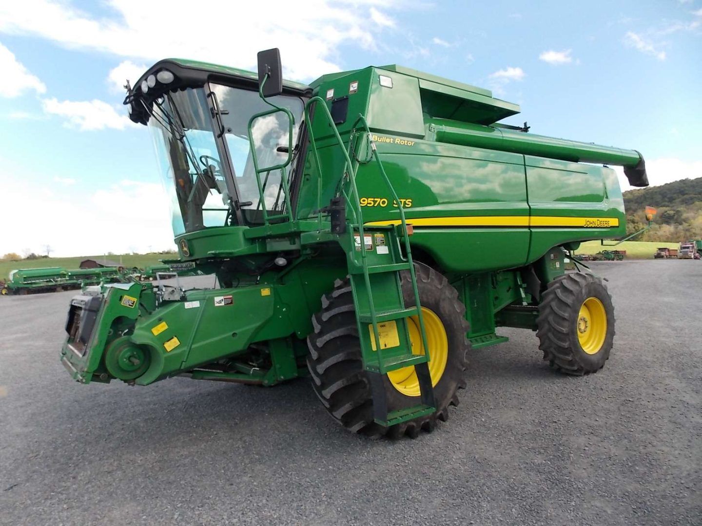 Green John Deere combine harvester parked on pavement under a blue sky