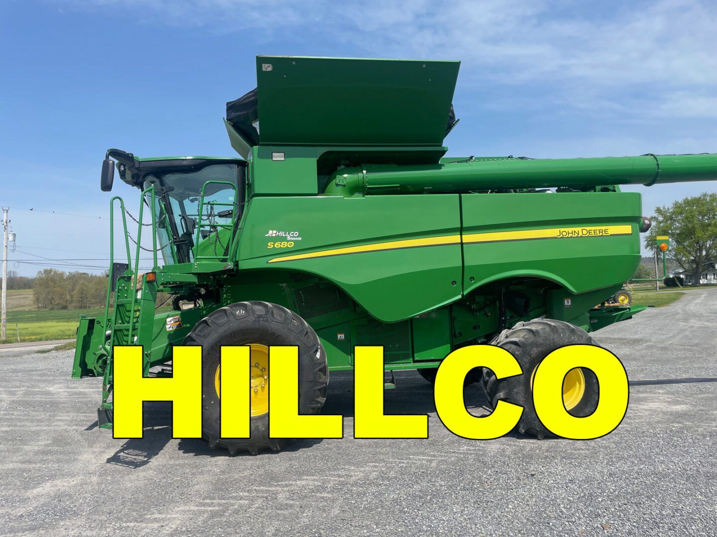 Green HILLCO combine harvester on a gravel lot under a clear blue sky