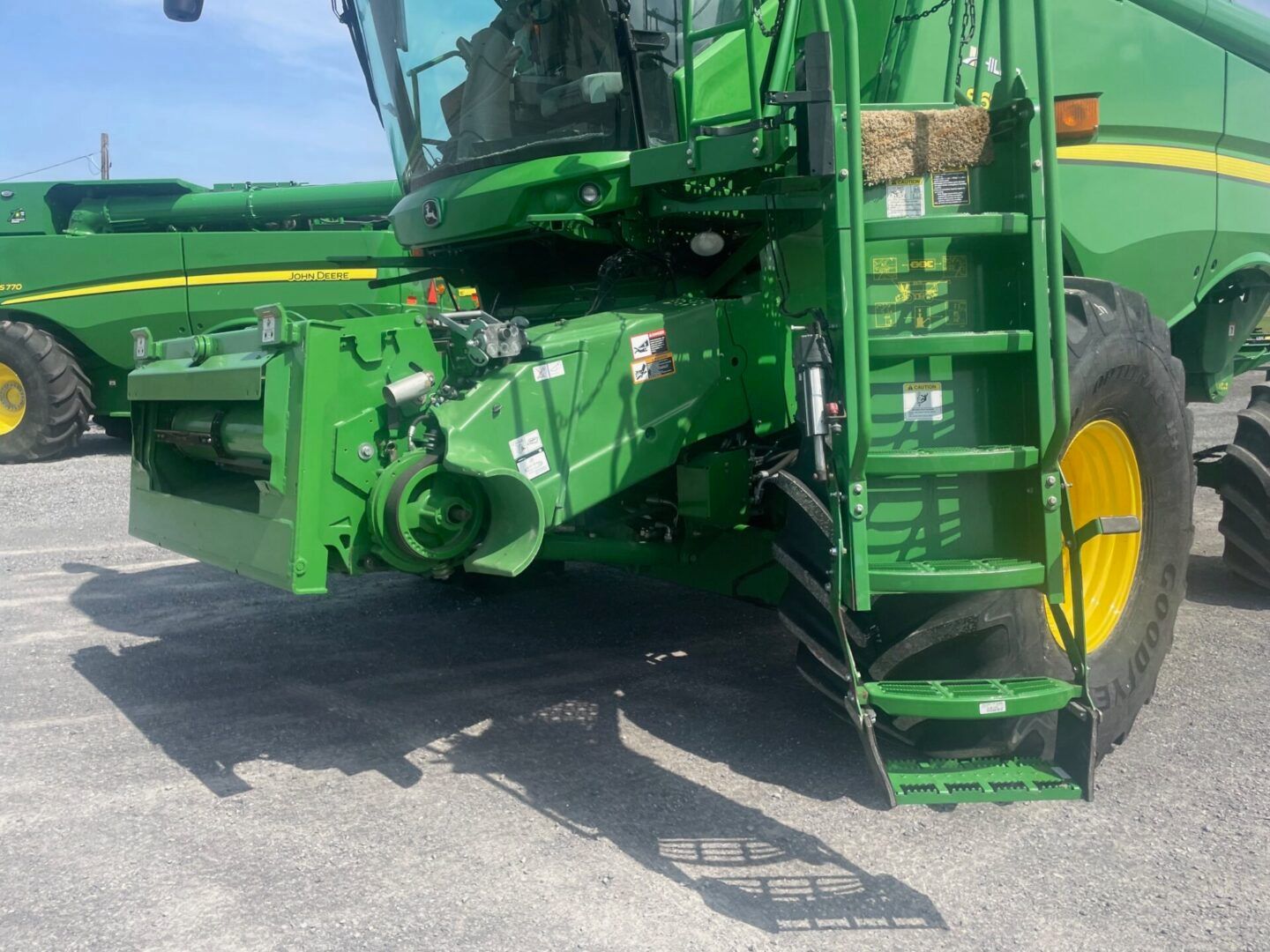 Green agricultural machine with yellow wheels parked on gravel, side view