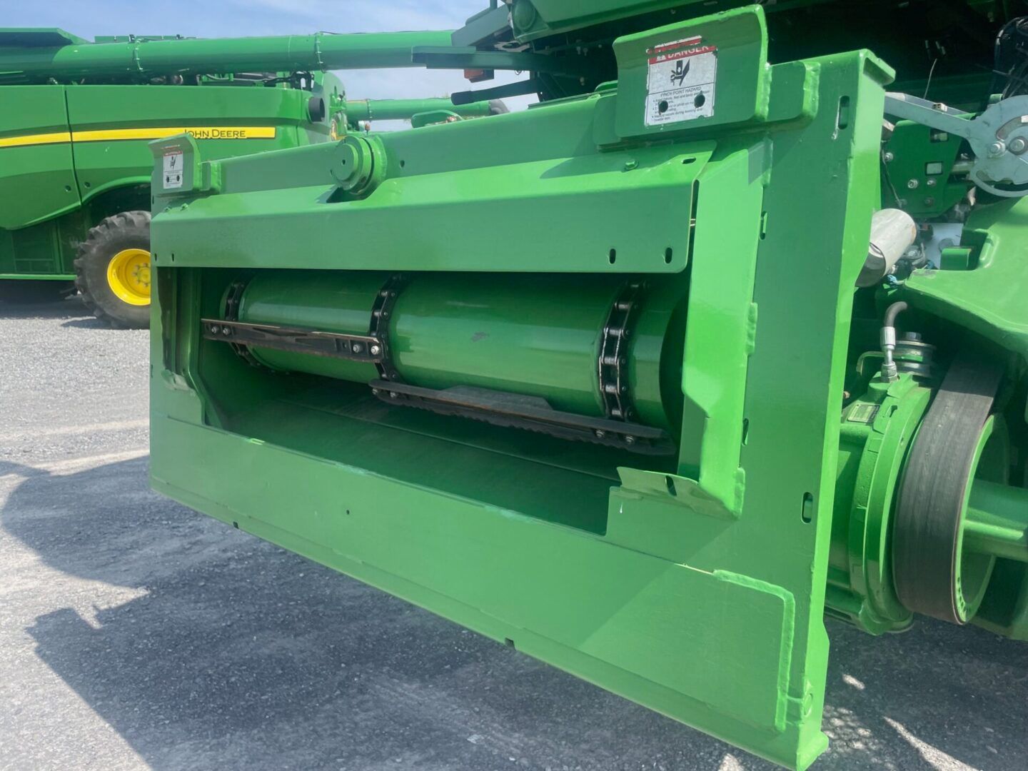Green agricultural machinery close-up with a cylindrical rotor and open side panel on pavement