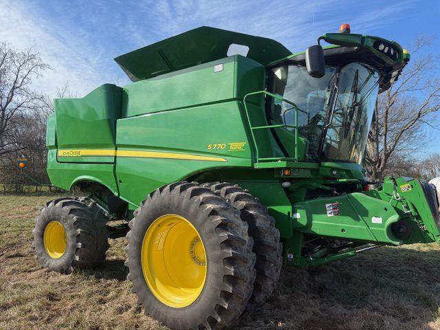 Green John Deere combine harvester with yellow wheels in a field under a cloudy sky