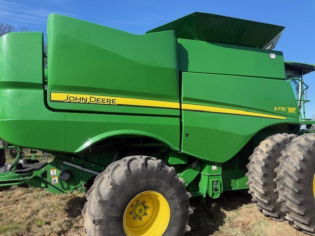 Green John Deere farm combine harvester with yellow wheels, parked in a field