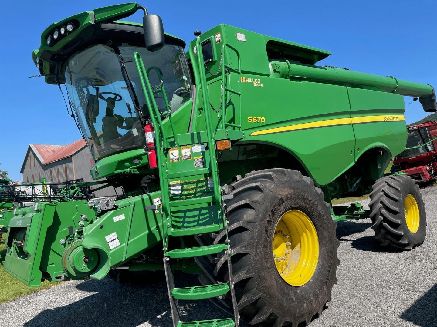 Green combine harvester on a gravel lot under a blue sky