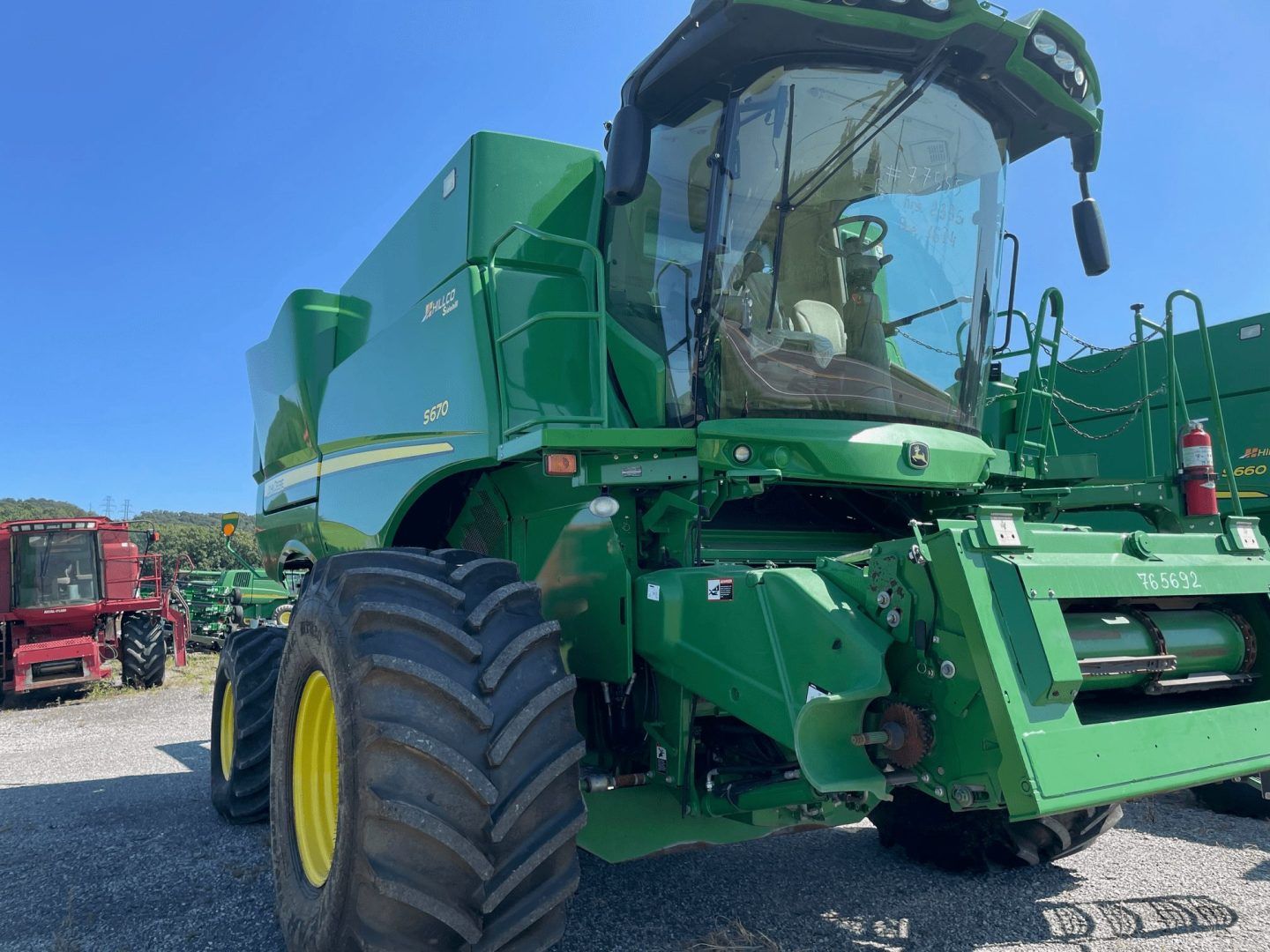 Green John Deere combine harvester parked on gravel under a blue sky