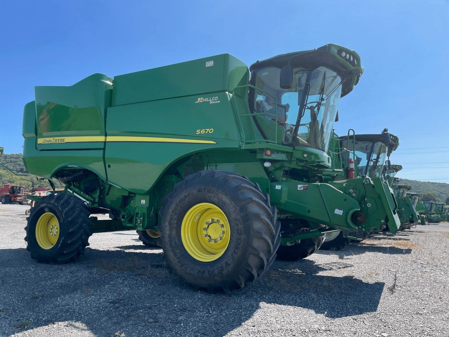 Green John Deere combine harvester parked on gravel under a blue sky.