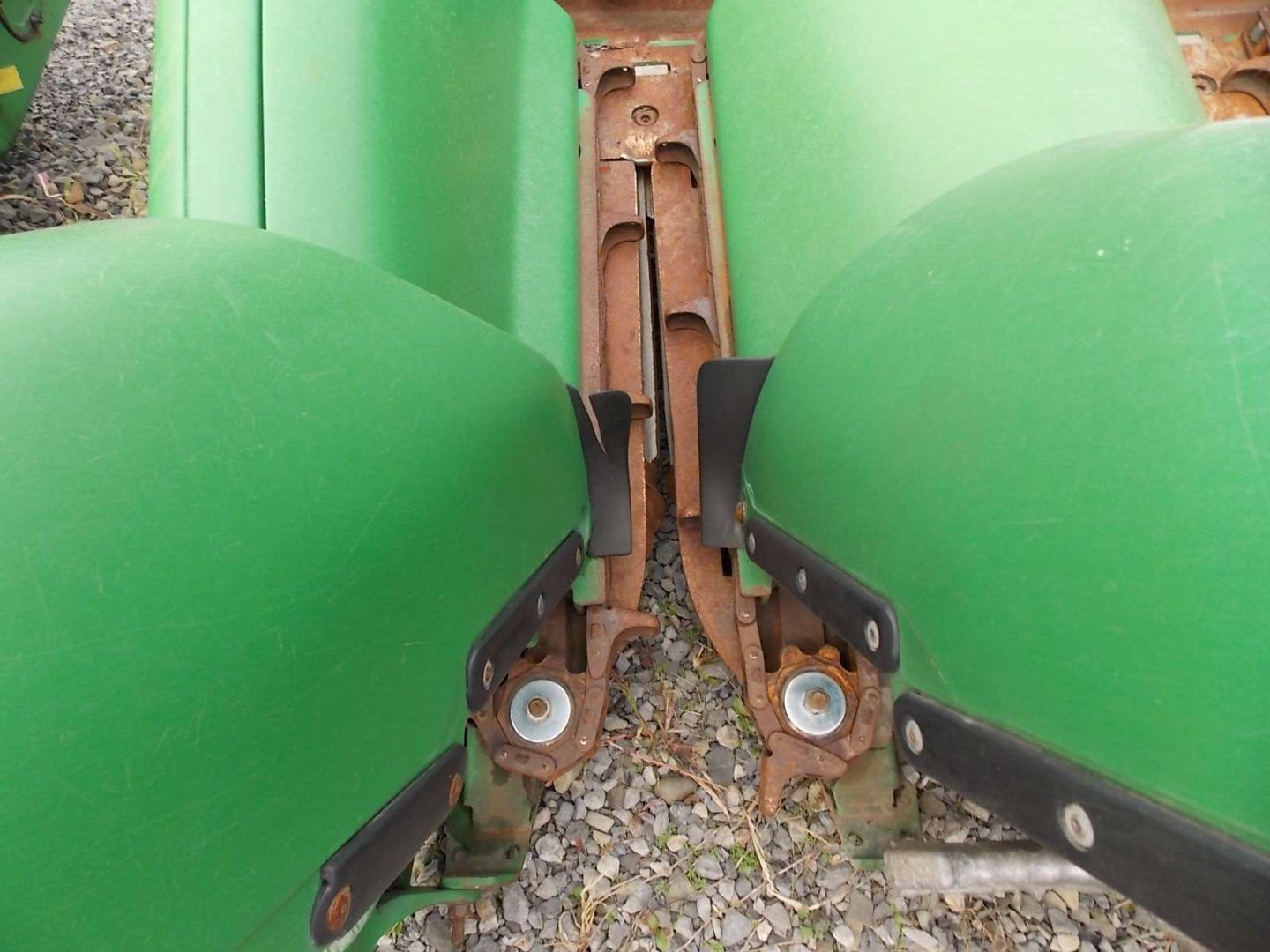 Close-up of green plastic bins connected by a rusty metal hinge over gravel.