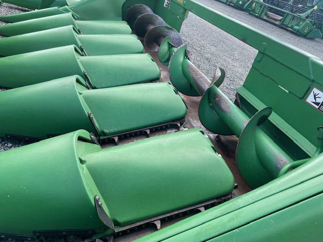 Green agricultural machine with rows of curved metal blades on a conveyor system
