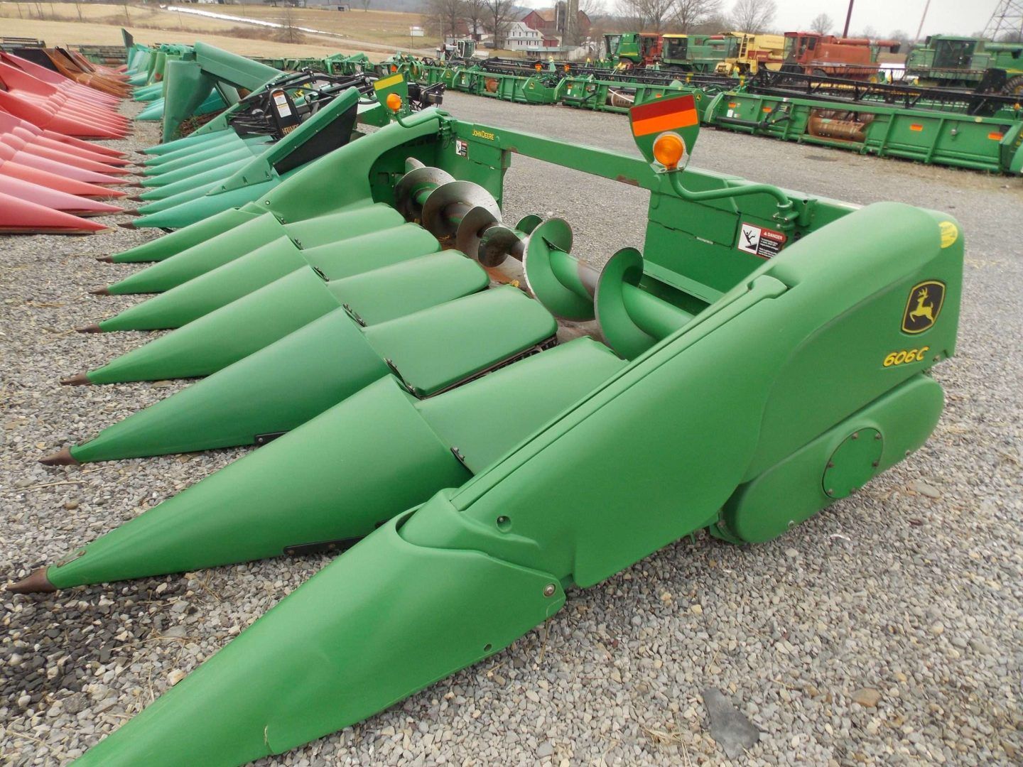 Green combine harvester corn headers lined up outdoors on gravel.