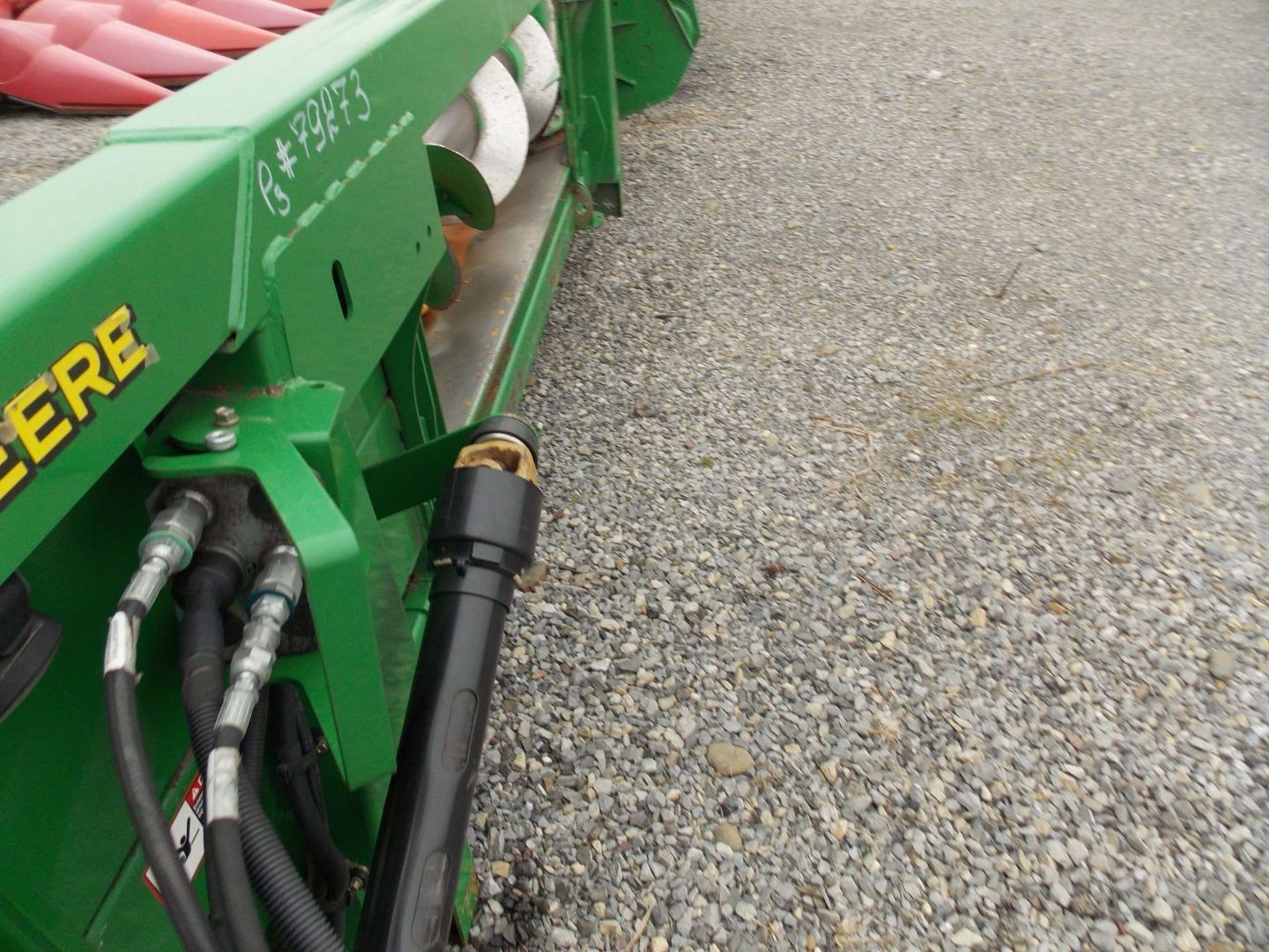 Green agricultural machine with black hydraulic hoses on a gravel surface