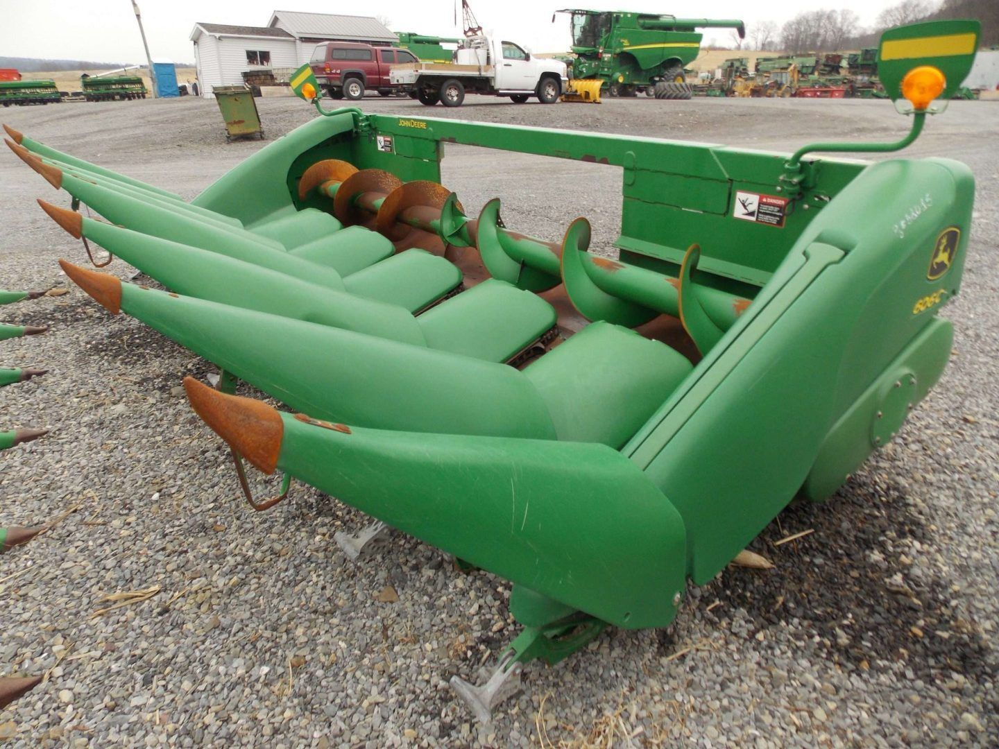 Green farm machinery attachment with pointed arms, parked on gravel lot
