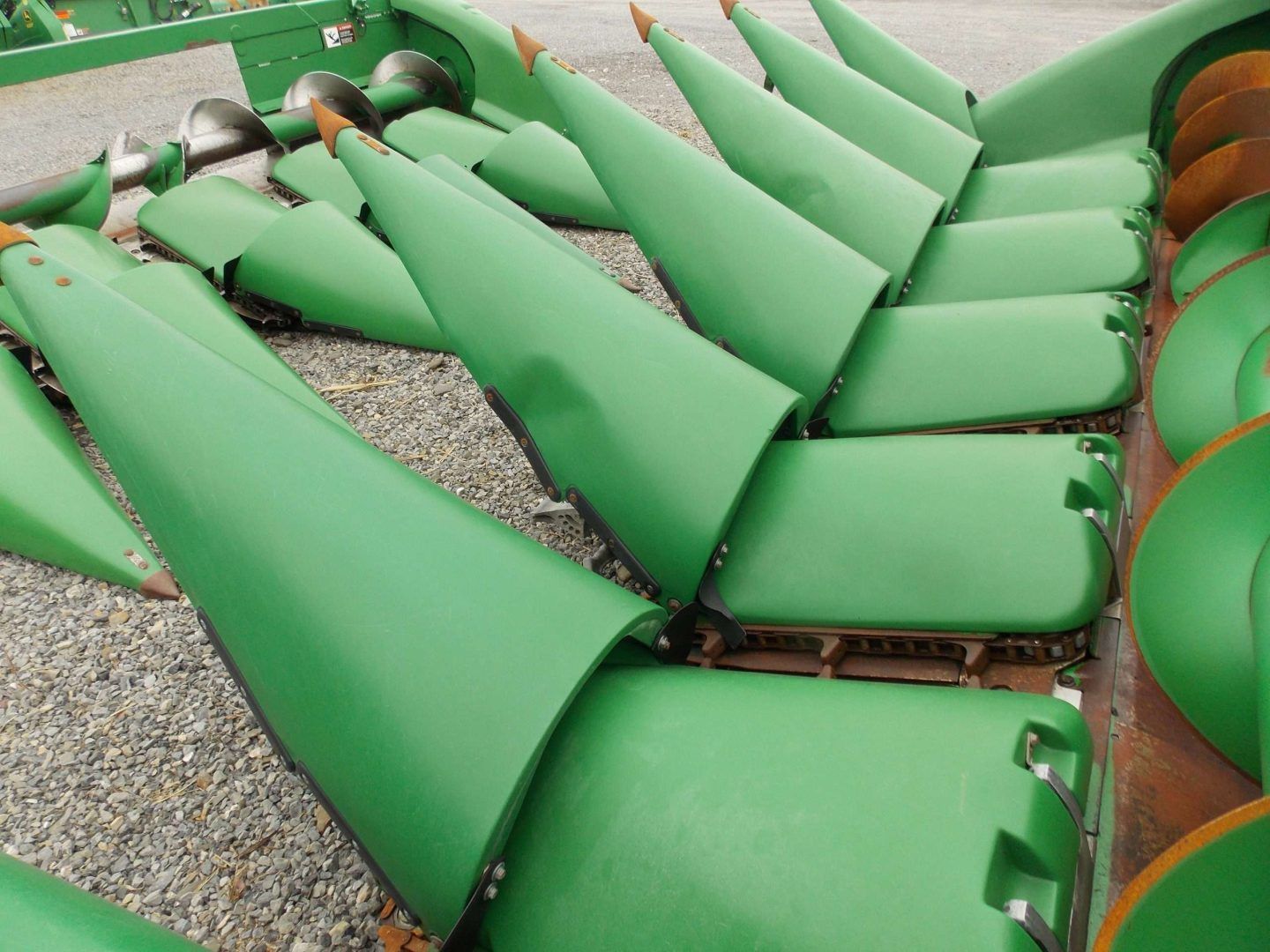 Green cylindrical industrial conveyor rollers on gravel, viewed from above in a factory or processing area.