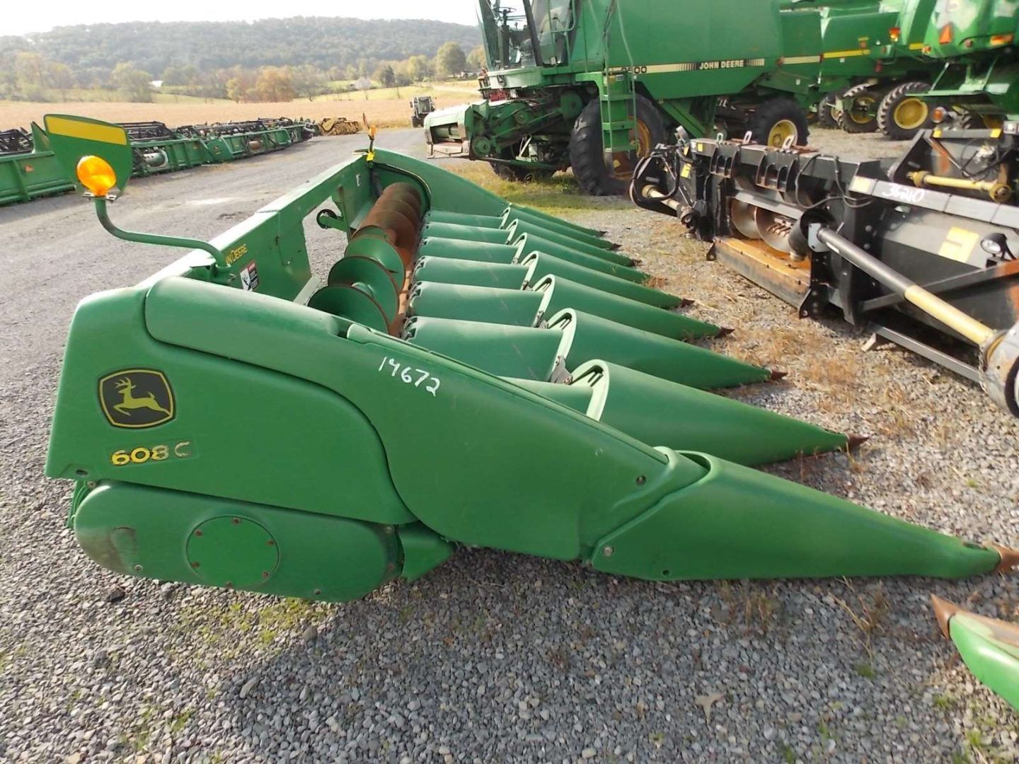 Green John Deere corn header on a gravel lot beside farm equipment