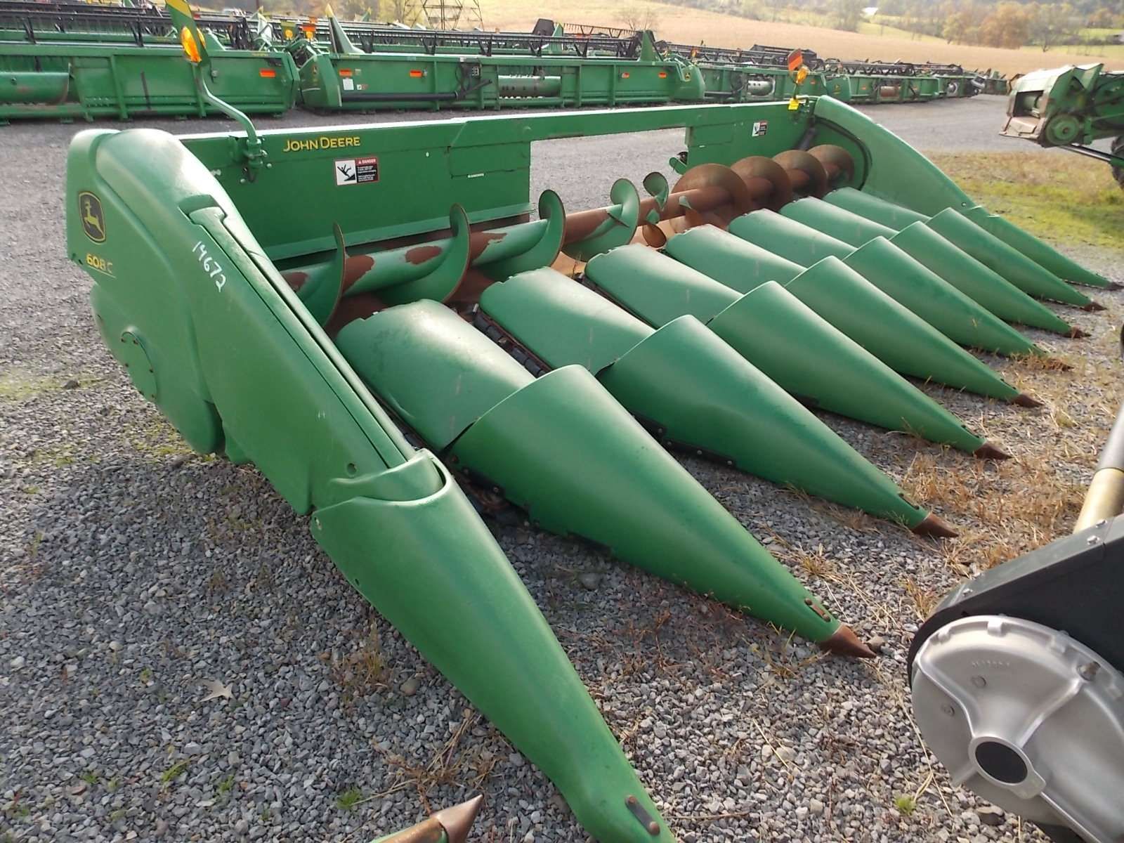 Green farm combine corn header with multiple pointed metal snouts parked outdoors on gravel