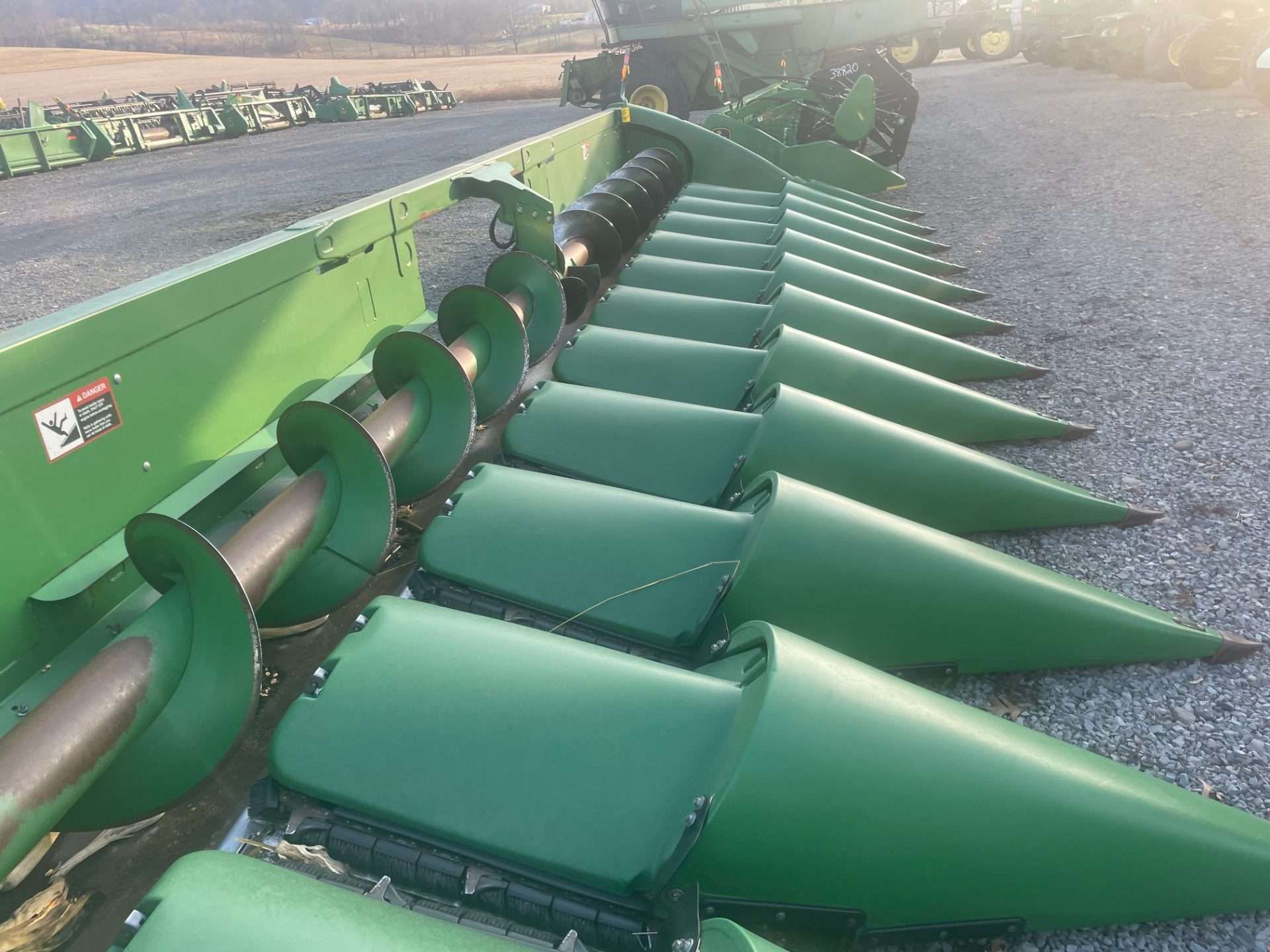 Green combine harvester header with rows of corn snouts in a gravel field