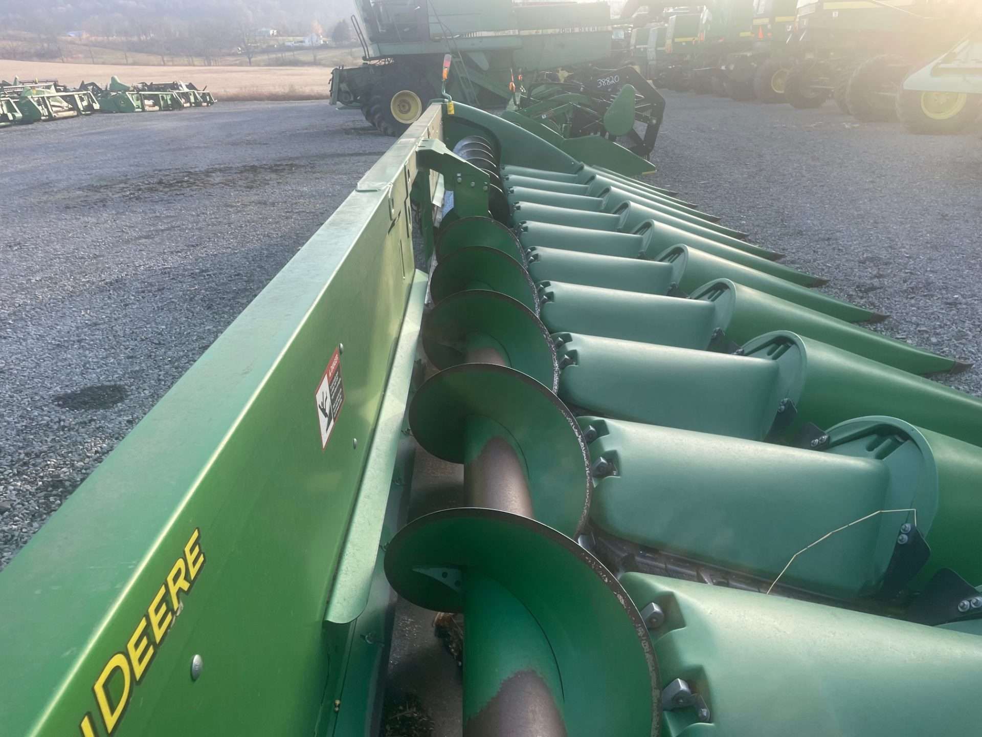 Green John Deere farm implement with row of rotating discs in a field, viewed from the front