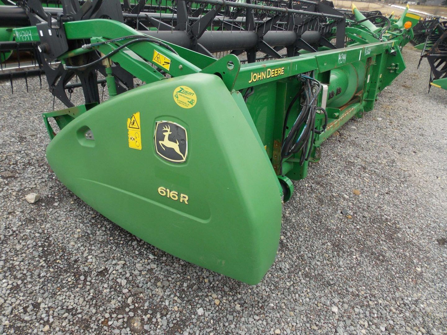 Green John Deere 916 H agricultural attachment on gravel lot, with black framework behind it