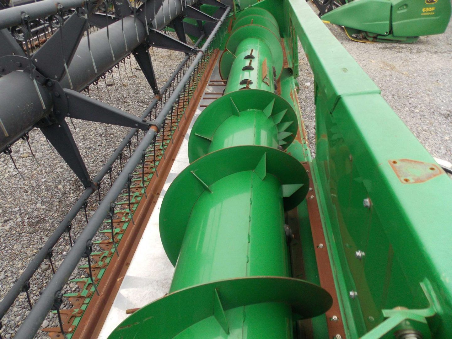 Green farm auger conveyor beside a black combine header in a field