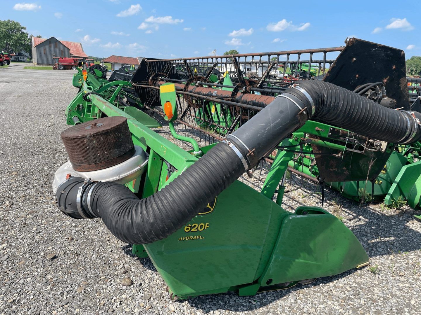 Green farm machine with black hoses parked on gravel in a rural yard